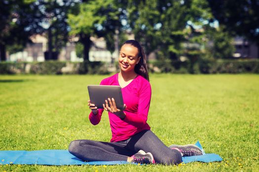 fitness, park, technology and sport concept - smiling african american woman with tablet pc computer sitting on mat outdoors