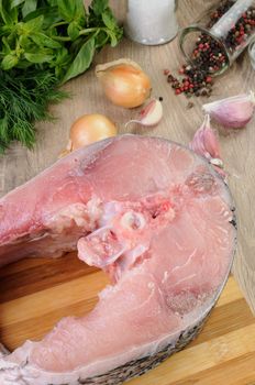 Raw piece (steak) carp on wooden board with fresh herbs and spices