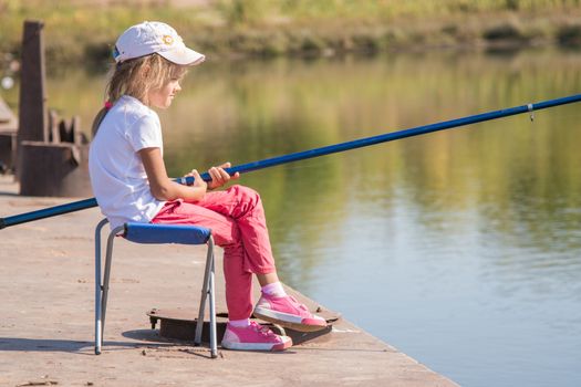 Six year old girl fishing from a bridge on a clear sunny day
