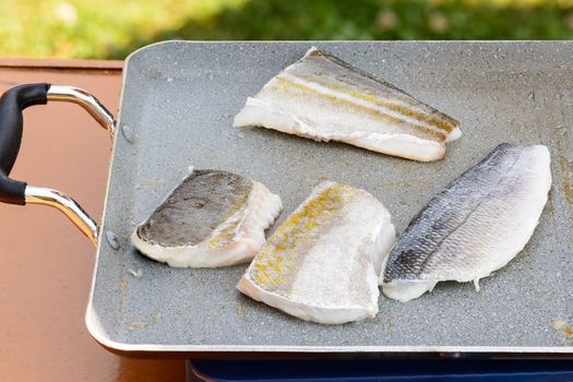 Pictured three fillets of sea bream and codfish cooked on the grill outdoor.