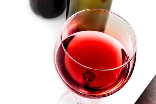 top of view of red wine glass near wine bottles on white table