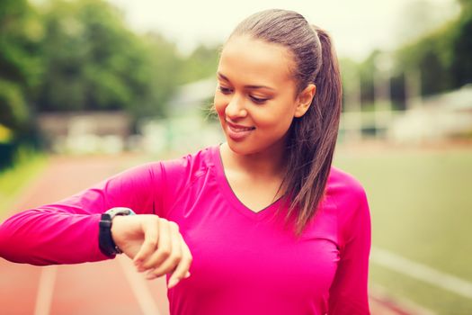 fitness, sport, training, technology and lifestyle concept - smiling african american woman with heart-rate watch on track outdoors