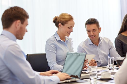 business, people and technology concept - smiling business team with laptop and tablet pc computer meeting in office