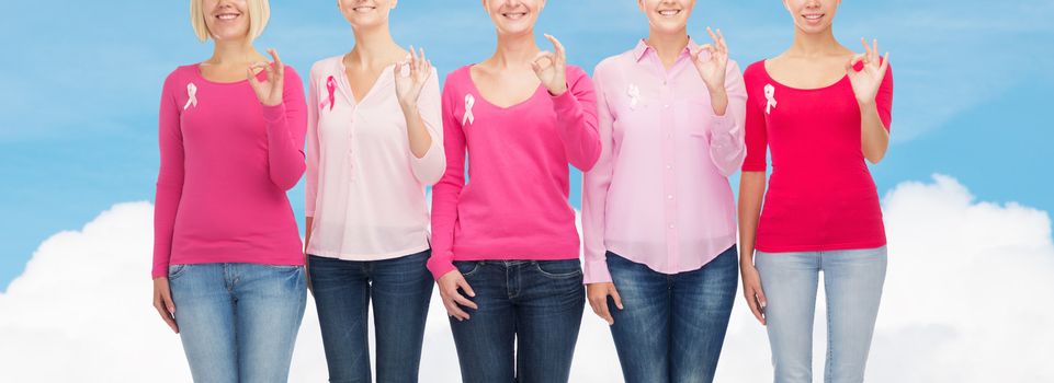 healthcare, people, gesture and medicine concept - close up of smiling women in blank shirts with pink breast cancer awareness ribbons showing ok sign over blue sky and white cloud background