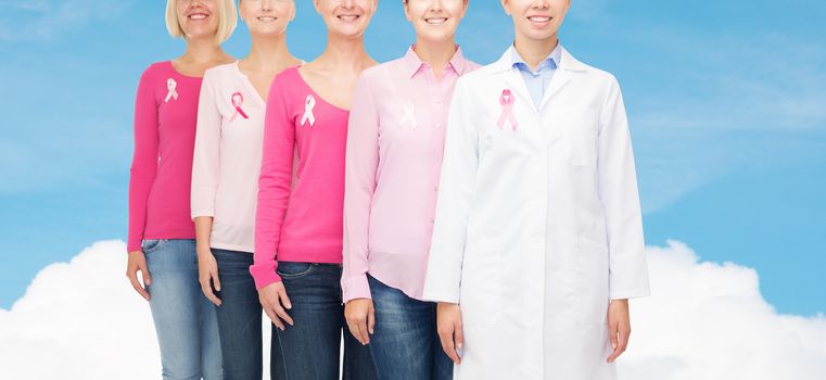 healthcare, people and medicine concept - close up of smiling women in blank shirts with pink breast cancer awareness ribbons over blue sky and white cloud background
