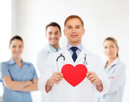 medicine, profession, charity and healthcare concept - smiling male doctor with red heart and stethoscope over group of medics