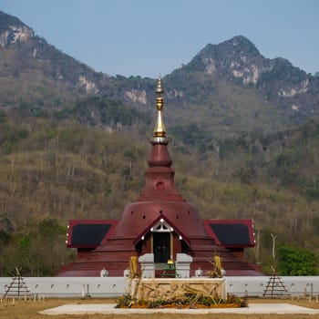 Kanchanaburi, Thailand - March 5, 2011 : red brown pagoda of Sunanthawararam Temple among the mountains 