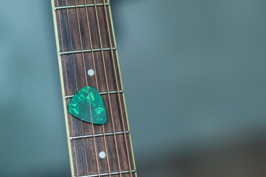 colorful green guitar pick on finger board, as abstract background