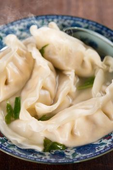 Close up fresh dumplings soup on plate with hot steams. Chinese cuisine on old vintage wooden background.