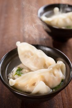 Fresh dumplings soup on plate with hot steams. Chinese cuisine on rustic old vintage wooden background.