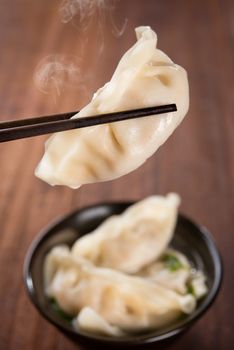 Fresh dumplings soup on plate with chopsticks and hot steams. Chinese dish on rustic old vintage wooden background.