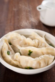 Fresh dumplings soup on plate with hot steams. Chinese food on rustic old vintage wooden background.