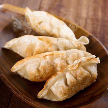 Fresh pan fried dumplings on plate with hot steams. Asian dish on rustic old vintage wooden background.