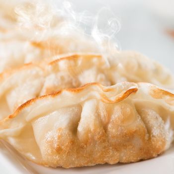 Close up fresh pan fried dumplings on plate with hot steams. Asian food on rustic vintage wooden background.