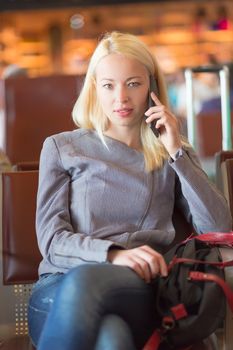 Casual blond young woman calling by cell phone while waiting to board a plane at the departure gates. Wireless network hotspot enabling people to access internet conection. Public transport.