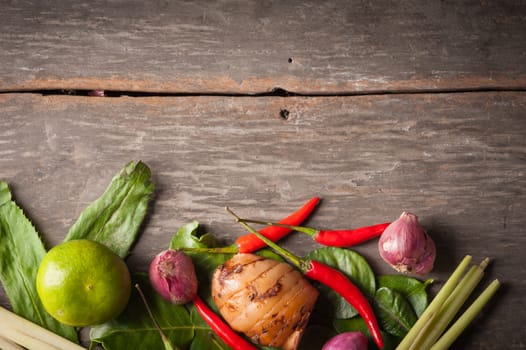Ingredients set for Thai spicy soup (Tom-yum) include lemon, galangal, red chili, red onion, lemongrass, and kaffir lime leaf on wood table in morning scene with blank area for text or message