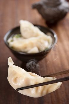 Fresh dumplings soup on plate with chopsticks and hot steams. Chinese cuisine on rustic old vintage wooden background.