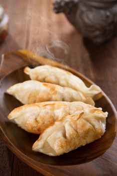 Fresh pan fried dumplings on plate with hot steams. Asian food on rustic old vintage wooden background.
