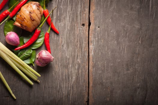 Ingredients set for Thai spicy soup (Tom-yum) include lemon, galangal, red chili, red onion, lemongrass, and kaffir lime leaf on wood table in morning scene with blank area for text or message