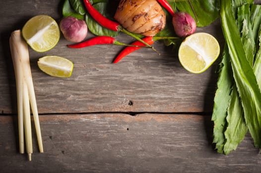 Ingredients set for Thai spicy soup (Tom-yum) include lemon, galangal, red chili, red onion, lemongrass, and kaffir lime leaf on wood table in morning scene with blank area for text or message