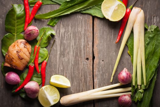 Ingredients set for Thai spicy soup (Tom-yum) include lemon, galangal, red chili, red onion, lemongrass, and kaffir lime leaf on wood table in morning scene with blank area for text or message