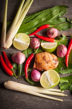 Ingredients set for Thai spicy soup (Tom-yum) include lemon, galangal, red chili, red onion, lemongrass, and kaffir lime leaf on wood table in morning scene