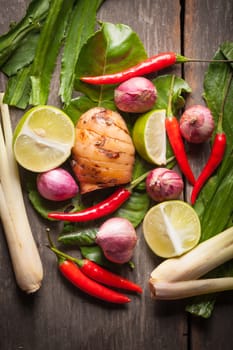 Ingredients set for Thai spicy soup (Tom-yum) include lemon, galangal, red chili, red onion, lemongrass, and kaffir lime leaf on wood table in morning scene