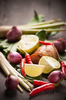Ingredients set for Thai spicy soup (Tom-yum) include lemon, galangal, red chili, red onion, lemongrass, and kaffir lime leaf on wood table in morning scene