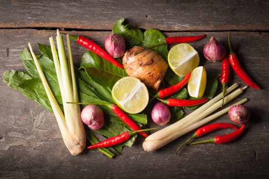 Ingredients set for Thai spicy soup (Tom-yum) include lemon, galangal, red chili, red onion, lemongrass, and kaffir lime leaf on wood table in morning scene