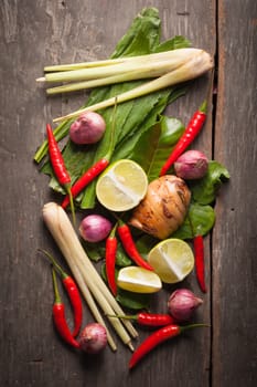 Ingredients set for Thai spicy soup (Tom-yum) include lemon, galangal, red chili, red onion, lemongrass, and kaffir lime leaf on wood table in morning scene