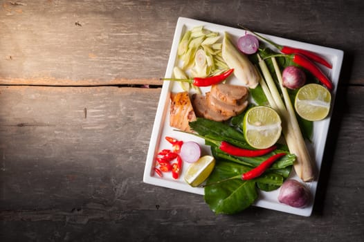 Ingredients set for Thai spicy soup (Tom-yum) include lemon, galangal, red chili, red onion, lemongrass, and kaffir lime leaf on wood table in morning scene with blank area for text or message