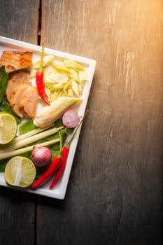 Ingredients set for Thai spicy soup (Tom-yum) include lemon, galangal, red chili, red onion, lemongrass, and kaffir lime leaf on wood table in morning scene with blank area for text or message
