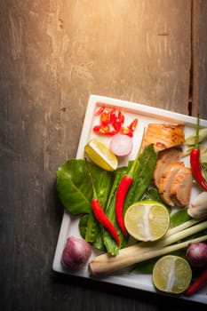 Ingredients set for Thai spicy soup (Tom-yum) include lemon, galangal, red chili, red onion, lemongrass, and kaffir lime leaf on wood table in morning scene