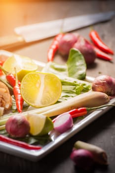 Ingredients set for Thai spicy soup (Tom-yum) include lemon, galangal, red chili, red onion, lemongrass, and kaffir lime leaf on wood table with low key scene