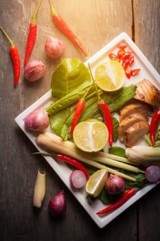 Ingredients set for Thai spicy soup (Tom-yum) include lemon, galangal, red chili, red onion, lemongrass, and kaffir lime leaf on wood table with morning scene