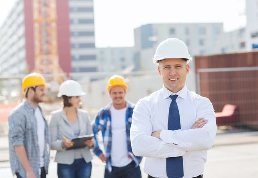 business, building, teamwork and people concept - group of smiling builders in hardhats outdoors