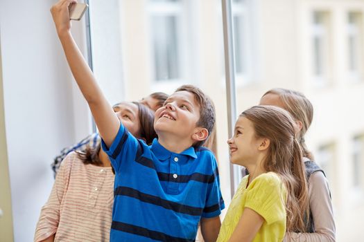 education, elementary school, drinks, children and people concept - group of school kids taking selfie with smartphone in corridor