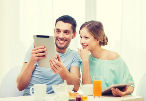 food, home, couple and technology concept - smiling couple with tablet pc reading news and having breakfast at home