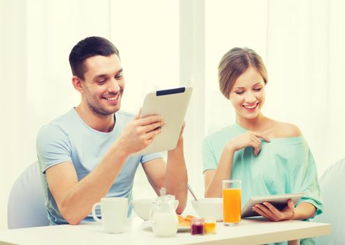 food, home, couple and technology concept - smiling couple with tablet pc reading news and having breakfast at home