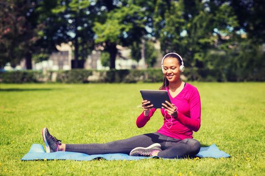 fitness, park, technology and sport concept - smiling african american woman with tablet pc computer and headphones on mat outdoors