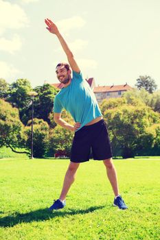 fitness, sport, training and lifestyle concept - smiling man stretching hand outdoors