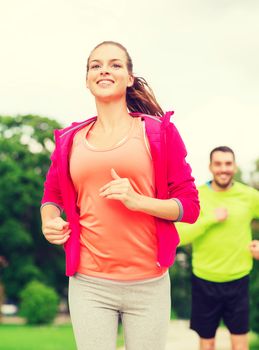 fitness, sport, friendship and lifestyle concept - smiling couple running outdoors