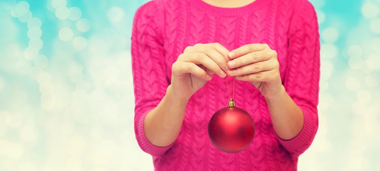 christmas, decoration, holidays and people concept - close up of woman in pink sweater holding christmas ball over blue lights background