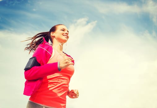 fitness, sport and lifestyle concept - smiling young woman with earphones running outdoors