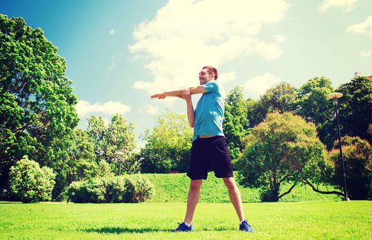 fitness, sport, training and lifestyle concept - smiling man stretching hand outdoors