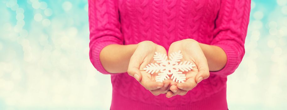 christmas, holidays and people concept - close up of woman in pink sweater holding snowflake over blue lights background