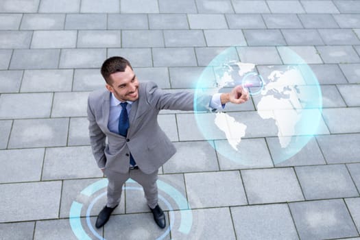 global business, development, technology and people and concept - young smiling businessman pointing finger to virtual globe projection outdoors from top