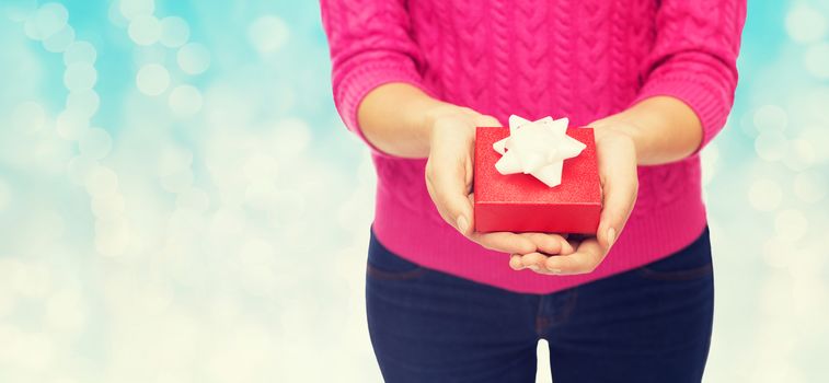 christmas, holidays and people concept - close up of woman in pink sweater holding gift box over blue lights background