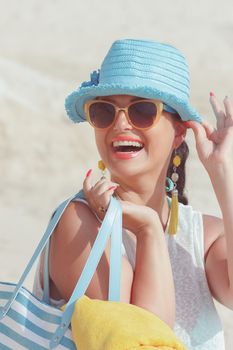 Beautiful woman smiling and carrying bag on the sandy beach. Summer vacation concept. Vintage style, selective focus