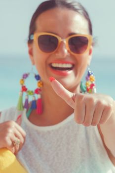 Beautiful young woman giving a thumbs up while at the beach. Focus on thumb